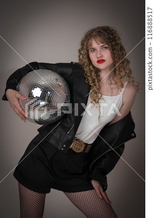 Confident hipster woman dancer holds mirror disco ball, gazing directly at camera. Woman exudes an air of sensuality, dressed in leather black jacket and shorts, during celebration of nightclub party Confident hipster woman dancer holds mirror disco ball, gazing directly at camera. Woman exudes an air of sensuality, dressed in leather black jacket and shorts, during celebration of nightclub party 116888517