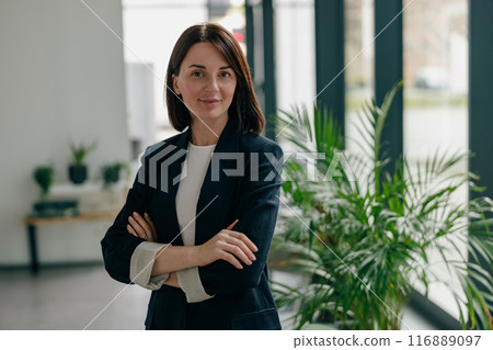 A confident, successful woman is standing in a sleek, contemporary office space A confident, successful woman is standing in a sleek, contemporary office space 116889097
