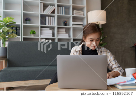 woman meticulously plans a finance audit, using a computer and calculator to review budget documents and ensure accuracy 116892167