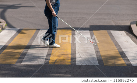 Close-up of the legs of a blind woman crossing the road at a crosswalk with a cane. Close-up of the legs of a blind woman crossing the road at a crosswalk with a cane. 116892270