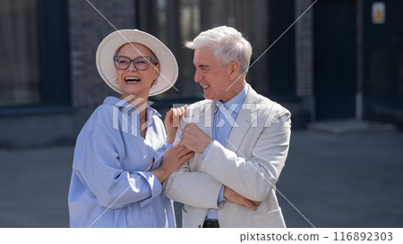 An elderly couple in love walks through the city. Portrait of a stylish gray-haired man and woman.  116892303