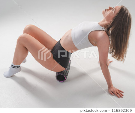 Caucasian woman doing roller exercise for myofascial release on white background. Self-massage of thighs.  116892369