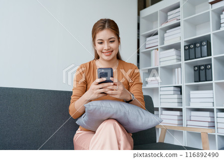 woman relaxation on a sofa, scrolling through social media on her smartphone 116892490
