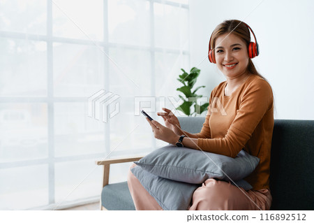 A woman feels utterly relaxed as she sits with her headphones, listening to music on her smartphone 116892512