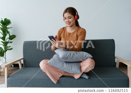 A woman feels utterly relaxed as she sits with her headphones, listening to music on her smartphone 116892515