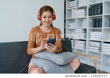 A woman feels utterly relaxed as she sits with her headphones, listening to music on her smartphone 116892517
