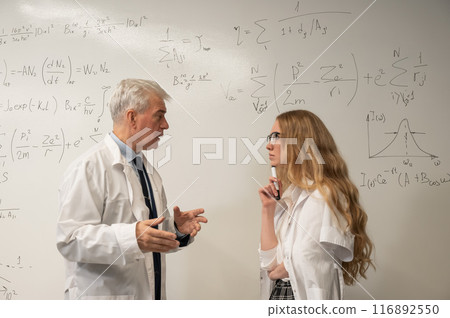 An elderly man and a young woman at a white board. Colleagues scientists discuss work issues.  116892550