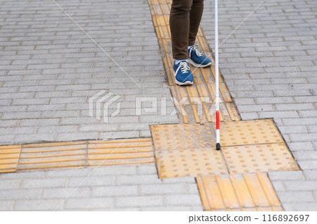 Close-up of a woman's legs with a cane near a tactile tile. Close-up of a woman's legs with a cane near a tactile tile. 116892697