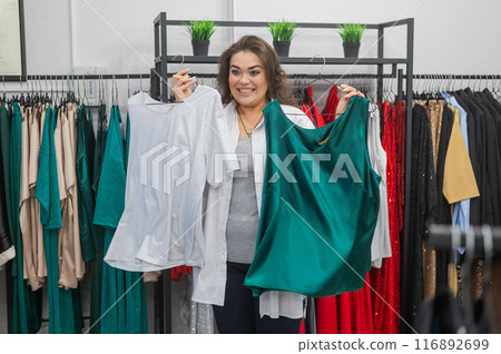 Smiling Caucasian fat woman choosing clothes. Plus size store. Smiling Caucasian fat woman choosing clothes. Plus size store. 116892699
