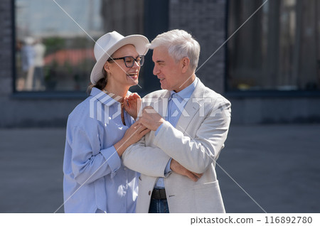 An elderly couple in love walks through the city. Portrait of a stylish gray-haired man and woman.  116892780