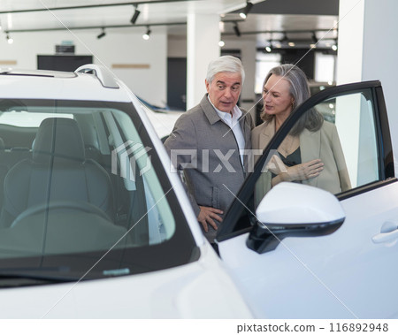 An elderly Caucasian couple chooses a new car at a car dealership. 116892948