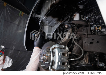 An auto mechanic applies anti-corrosion mastic to the underbody of a car. An auto mechanic applies anti-corrosion mastic to the underbody of a car. 116892953
