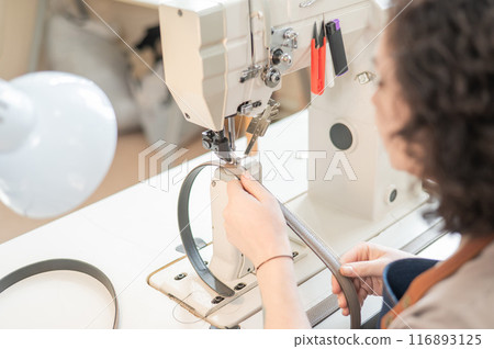 A woman tanner sews a leather belt on a sewing machine. Close-up of hands. A woman tanner sews a leather belt on a sewing machine. Close-up of hands. 116893125