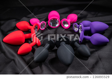 A set of silicone anal plugs in different colors and sizes on a black silk sheet. A set of silicone anal plugs in different colors and sizes on a black silk sheet. 116893329