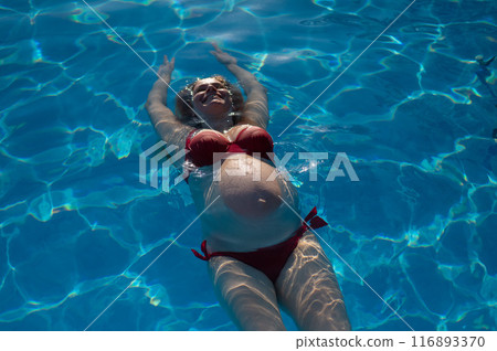 Top view of pregnant woman floating in pool in red bikini. Top view of pregnant woman floating in pool in red bikini. 116893370