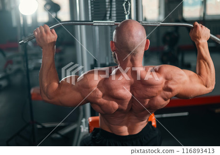 Caucasian man doing lat pull-downs on a machine. Caucasian man doing lat pull-downs on a machine. 116893413