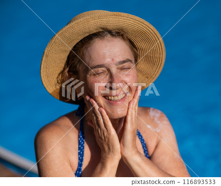 Portrait of an older woman applying sunscreen to her face while on vacation.  116893533
