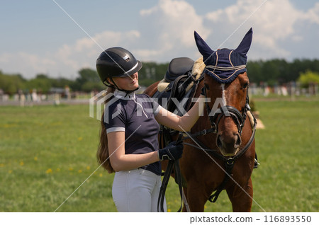 A young girl stands next to a horse before an equestrian competition.  116893550