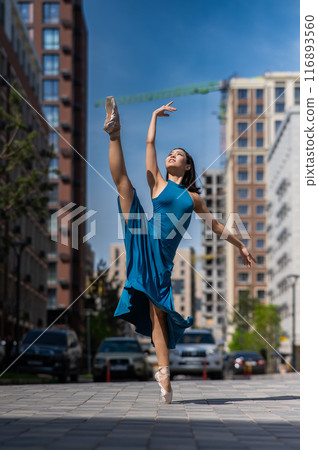 Beautiful Asian ballerina in blue dress posing in splits outdoors. Urban landscape. Vertical photo.  116893560