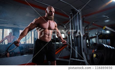 Bald Caucasian bodybuilder training chest using cable crossover in gym. Bald Caucasian bodybuilder training chest using cable crossover in gym. 116893650