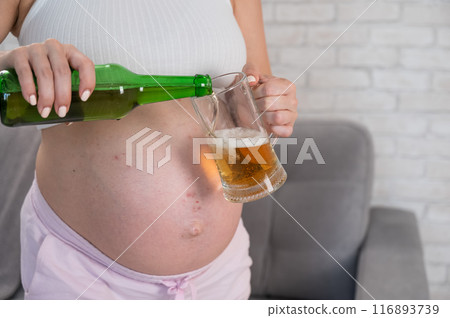 Faceless pregnant woman pouring beer into a glass.  116893739
