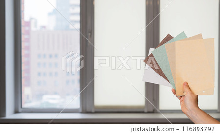 Woman holding fabric samples of roller blinds against window background.  116893792