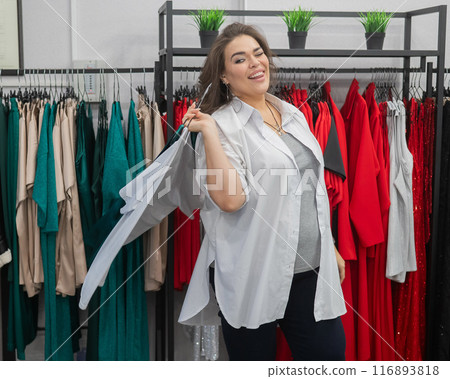 Smiling Caucasian fat woman choosing clothes. Plus size store. Smiling Caucasian fat woman choosing clothes. Plus size store. 116893818