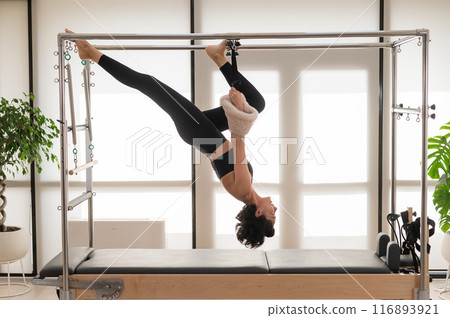 Asian woman doing aerial exercise on reformer machine.  116893921