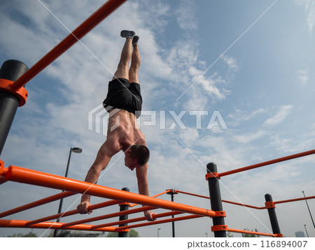 A young man doing a handstand on an outdoor sports field. Workout.  116894007