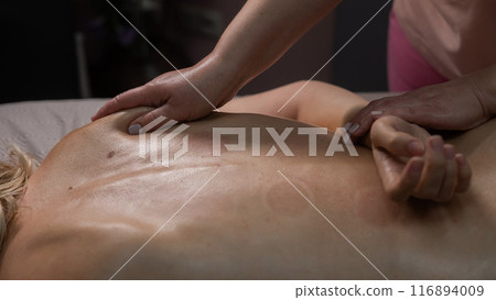 Woman having a therapeutic back massage. The masseur kneads the muscles under the shoulder blade.  Woman having a therapeutic back massage. The masseur kneads the muscles under the shoulder blade.  116894009