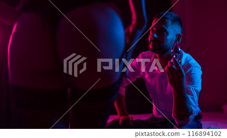 Bearded caucasian man holding an anal plug. Close-up of female buttocks in underwear. Sexual preferences of the couple. 116894102