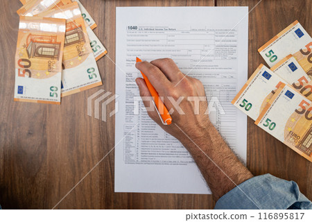 Agricultural worker completes 1040 tax form with pen in hand detailing seasonal earnings and travel expenses to determine tax liability sitting at table with euro bills 116895817