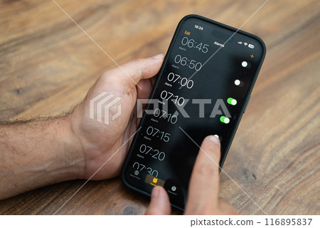 Male person holds modern smartphone setting time on alarm clock app ensuring to receive timely notifications to wake up early in morning for productive working day 116895837