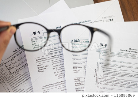 Male hand holds glasses above different tax forms mandatory for taxpayers to report annual income and financial information to avoid penalties from government Male hand holds glasses above different tax forms mandatory for taxpayers to report annual income and financial information to avoid penalties from government 116895869
