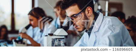 Male scientist using microscope in lab with colleagues in background. Collaboration and teamwork in scientific research. 116896605