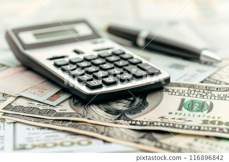 Close-up of a calculator and pen on top of US dollar bills. Financial calculations and budget planning for tax day, tax refunds, or accounting purposes. 116896842