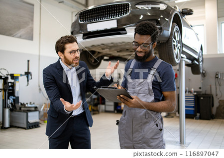 Customer discussing car repair details with mechanic in service center Customer discussing car repair details with mechanic in service center 116897047