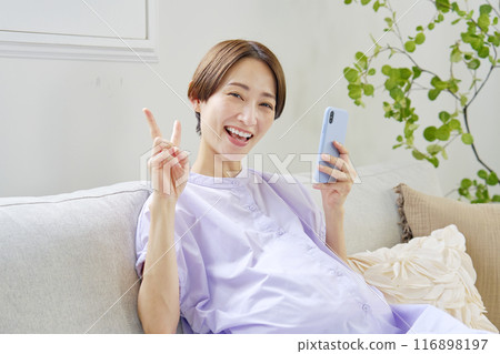 A pregnant woman with advanced pregnancy making a peace sign with a smartphone at home A pregnant woman with advanced pregnancy making a peace sign with a smartphone at home 116898197