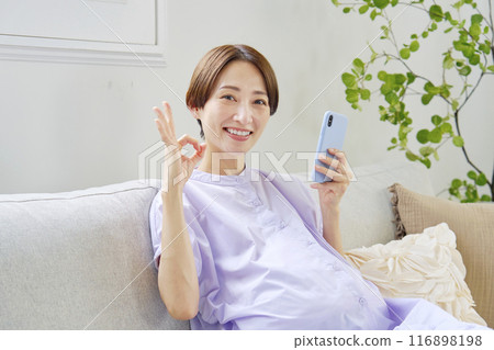 A pregnant woman with advanced pregnancy making an OK sign with a smartphone at home A pregnant woman with advanced pregnancy making an OK sign with a smartphone at home 116898198