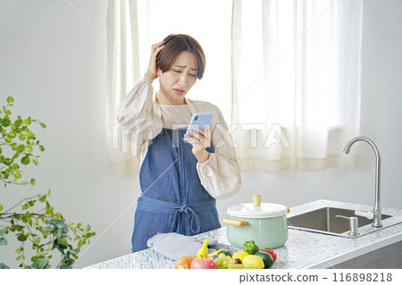 一位女士一邊在廚房擔心一邊看著智慧型手機 116898218