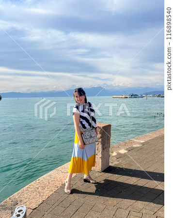 Woman in long dress enjoying stunning view over the Garda lake, seen from Peschiera del Garda 116898540
