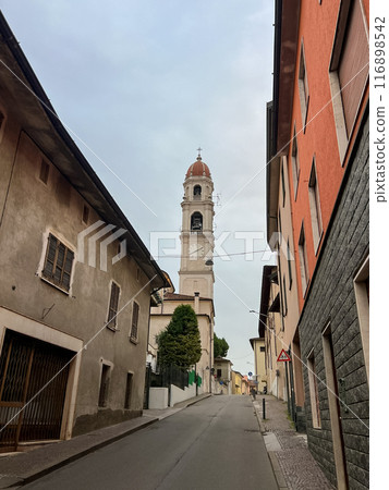 Pontevico, Italy. Deserted street in an italian town with old houses and belfry of old church Pontevico, Italy. Deserted street in an italian town with old houses and belfry of old church 116898542