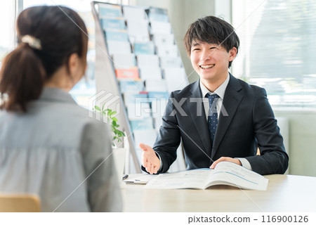 Young Asian businessman negotiating business with a female customer using a pamphlet/catalog (car/insurance) Young Asian businessman negotiating business with a female customer using a pamphlet/catalog (car/insurance) 116900126