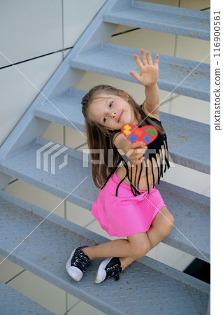 Cute little stylish girl shows a heart made of colorful puzzles for children with autism. Cute little stylish girl shows a heart made of colorful puzzles for children with autism. 116900561