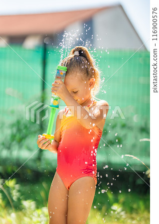 Little girl joyfully plays with water outside on a sunny day, abnormal heat in the city, water as a way to cool down in hot weather 116900576