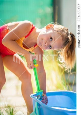Little girl joyfully plays with water outside on a sunny day, abnormal heat in the city, water as a way to cool down in hot weather 116900577