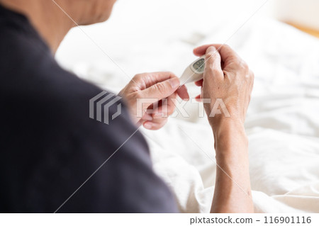 Man touching a thermometer on his bed 116901116