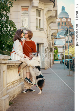 Flirting couple sitting on curb with their Aussie dog. Pet raining and city walking. Vertical 116901907
