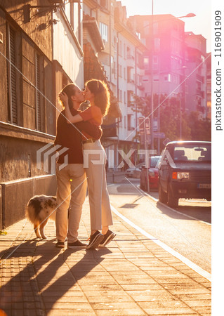 Romantic couple kissing on the street. Family walking with dog pet. Sunset light in background. Vertical orientation Romantic couple kissing on the street. Family walking with dog pet. Sunset light in background. Vertical orientation 116901909