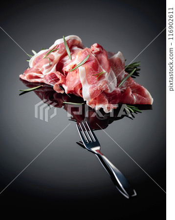 Italian prosciutto or Spanish jamon with rosemary on a black background. Italian prosciutto or Spanish jamon with rosemary on a black background. 116902611